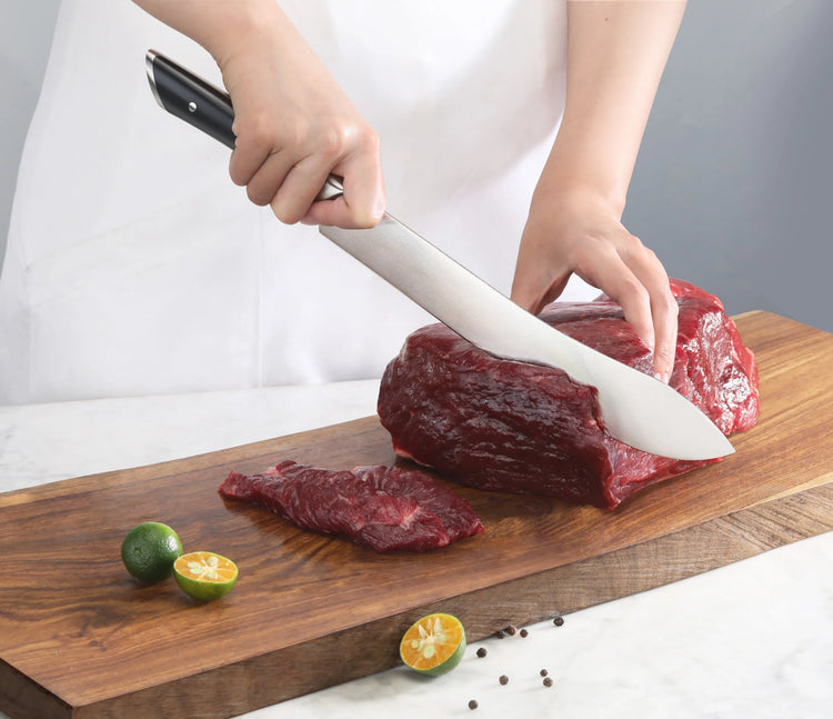 Person slicing raw beef on wooden cutting board with a large black-handled butcher knife.