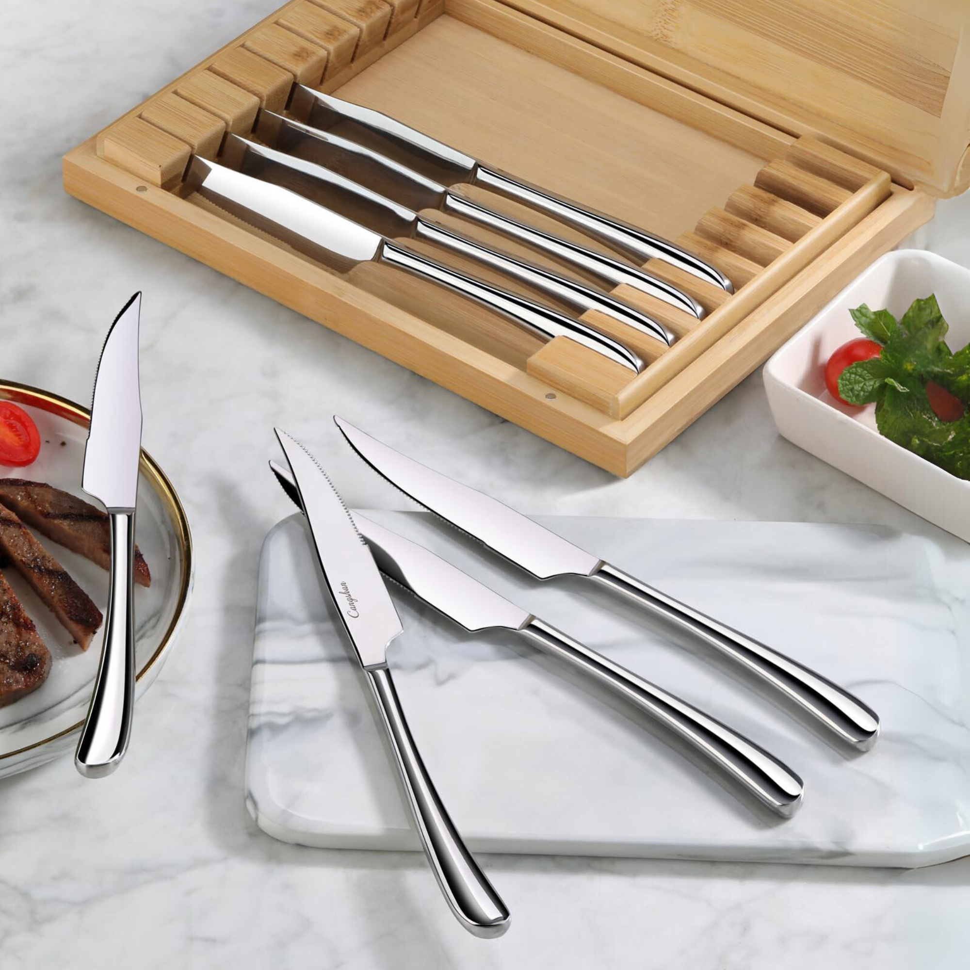 Set of eight stainless steel steak knives with curved handles, displayed in a bamboo storage box and on a marble surface.