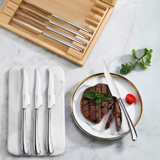 
                    
                      Eight stainless steel steak knives in a bamboo box, with three knives on a tray and one cutting a steak on a plate.
                    
                  