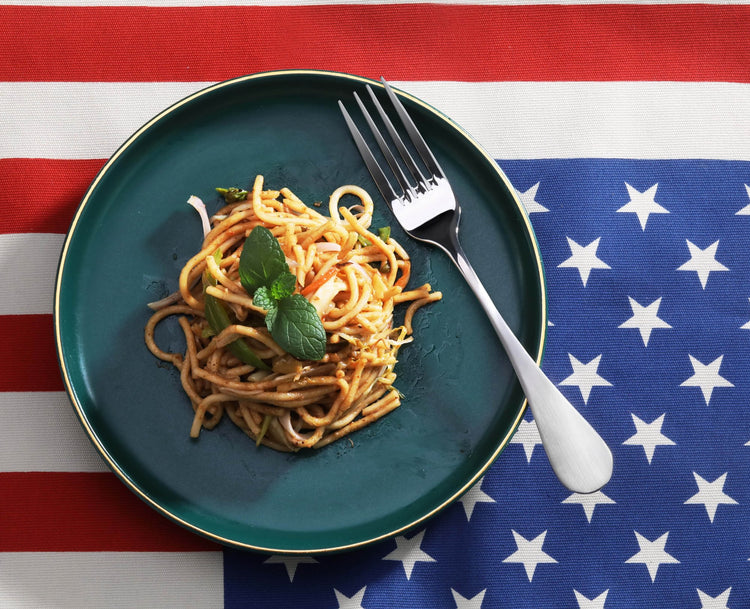 Dinner fork with matte finish handles resting on a green plate with spaghetti and basil, on an American flag background.