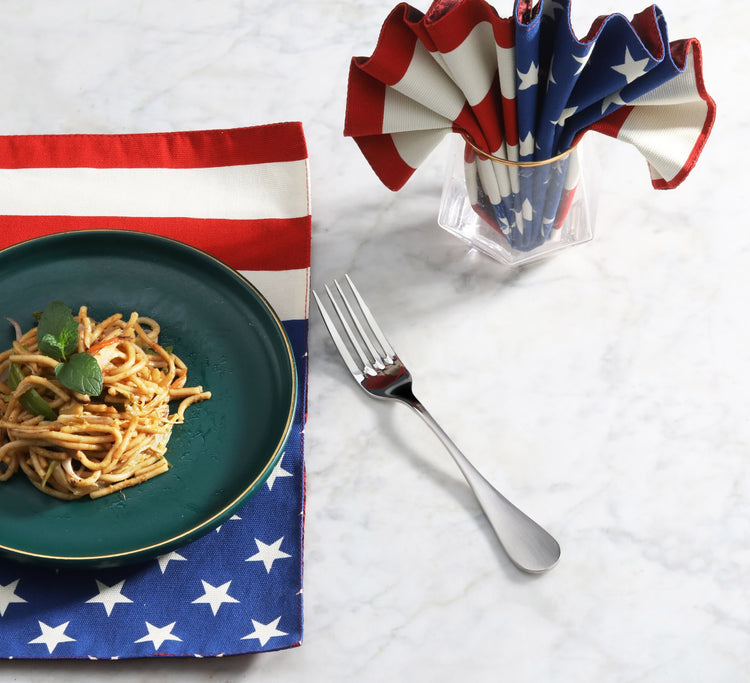 Single stainless steel dinner fork with matte finish handles placed on a white marble surface next to a plate of spaghetti an