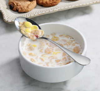 
                    
                      Stainless steel teaspoon with matte finish handles holding cereal and milk above a white bowl of cereal and milk.
                    
                  