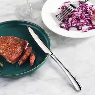 
                    
                      Polished stainless steel dinner knife resting on a green plate with sliced steak, next to a white plate with purple cabbage s
                    
                  