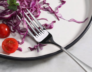 
                    
                      Salad fork with matte finish handle resting on a white plate with sliced red cabbage and cherry tomatoes.
                    
                  