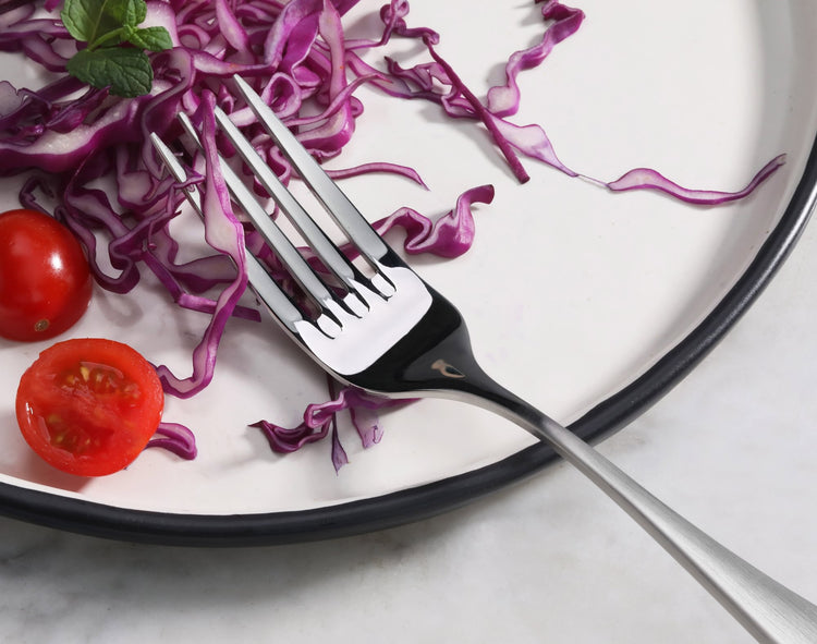 Salad fork with matte finish handle resting on a white plate with sliced red cabbage and cherry tomatoes.