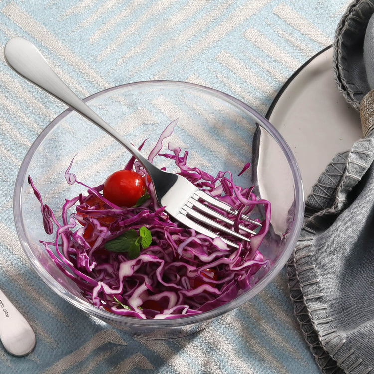Salad fork with matte finish handle resting in a glass bowl with shredded red cabbage and a cherry tomato.