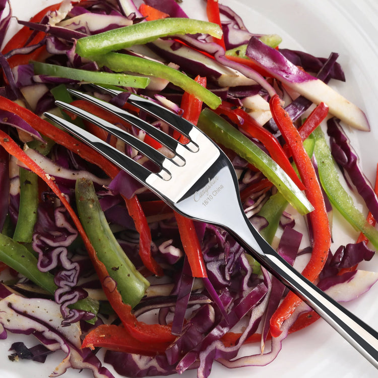 Fork with mirror finish resting on a plate of mixed sliced red cabbage, green beans, and red bell peppers.