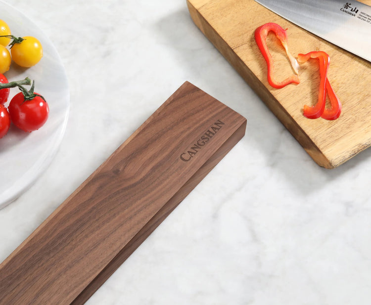 Walnut magnetic knife bar on marble countertop next to cutting board with sliced red bell pepper and knife.
