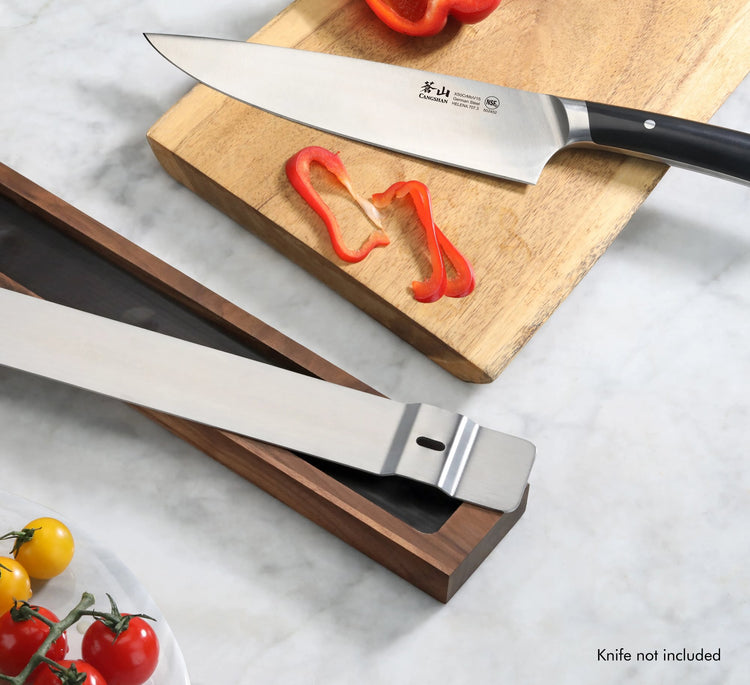 Walnut magnetic knife bar holding a large kitchen knife above a cutting board with sliced red bell pepper.