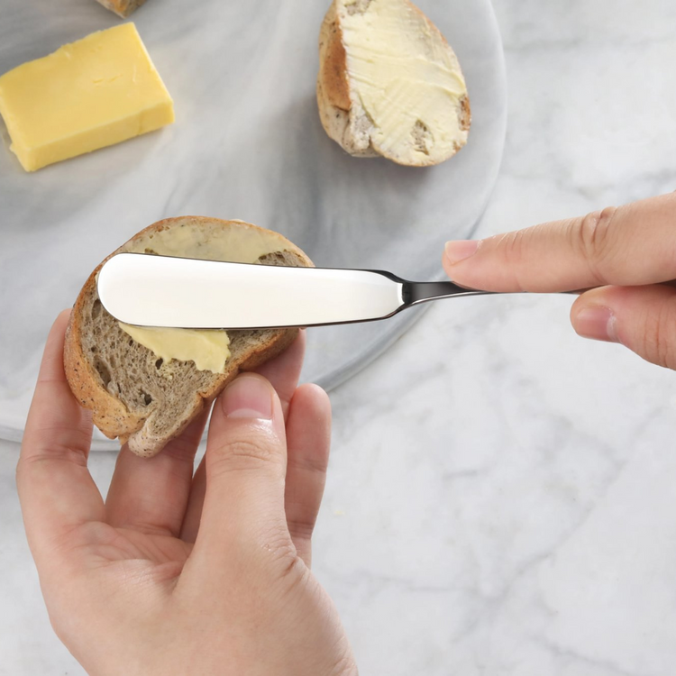 Hand spreading butter on bread slice using a stainless steel butter knife with matte finish handle.
