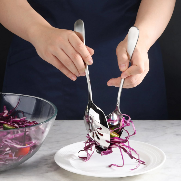 Hands using a stainless steel slotted serving spoon and spoon to serve shredded purple cabbage onto a white plate.