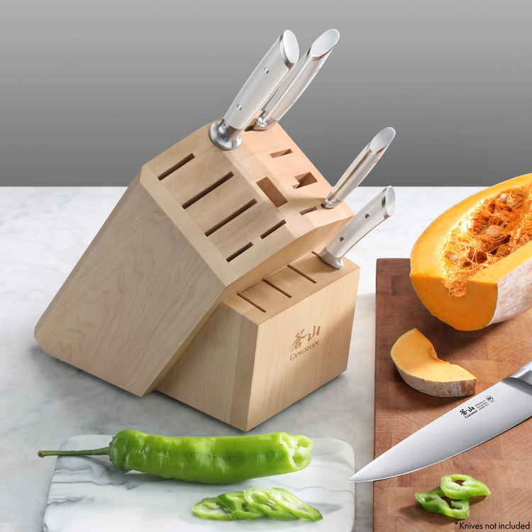 Maple knife block with 16 slots, holding four knives with white handles, next to sliced green pepper and pumpkin.