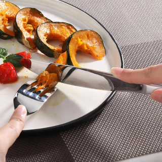 
                    
                      Hands using a stainless steel dinner knife and fork to cut roasted pumpkin slices on a white plate.
                    
                  