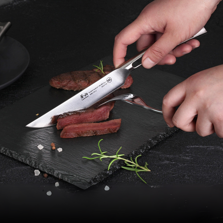 Hands slicing medium-rare steak on a black slate plate using a stainless steel steak knife and fork.