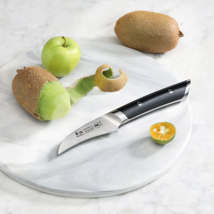 Peeling knife with black handle on marble board next to peeled kiwi, green apple, and halved kumquat.