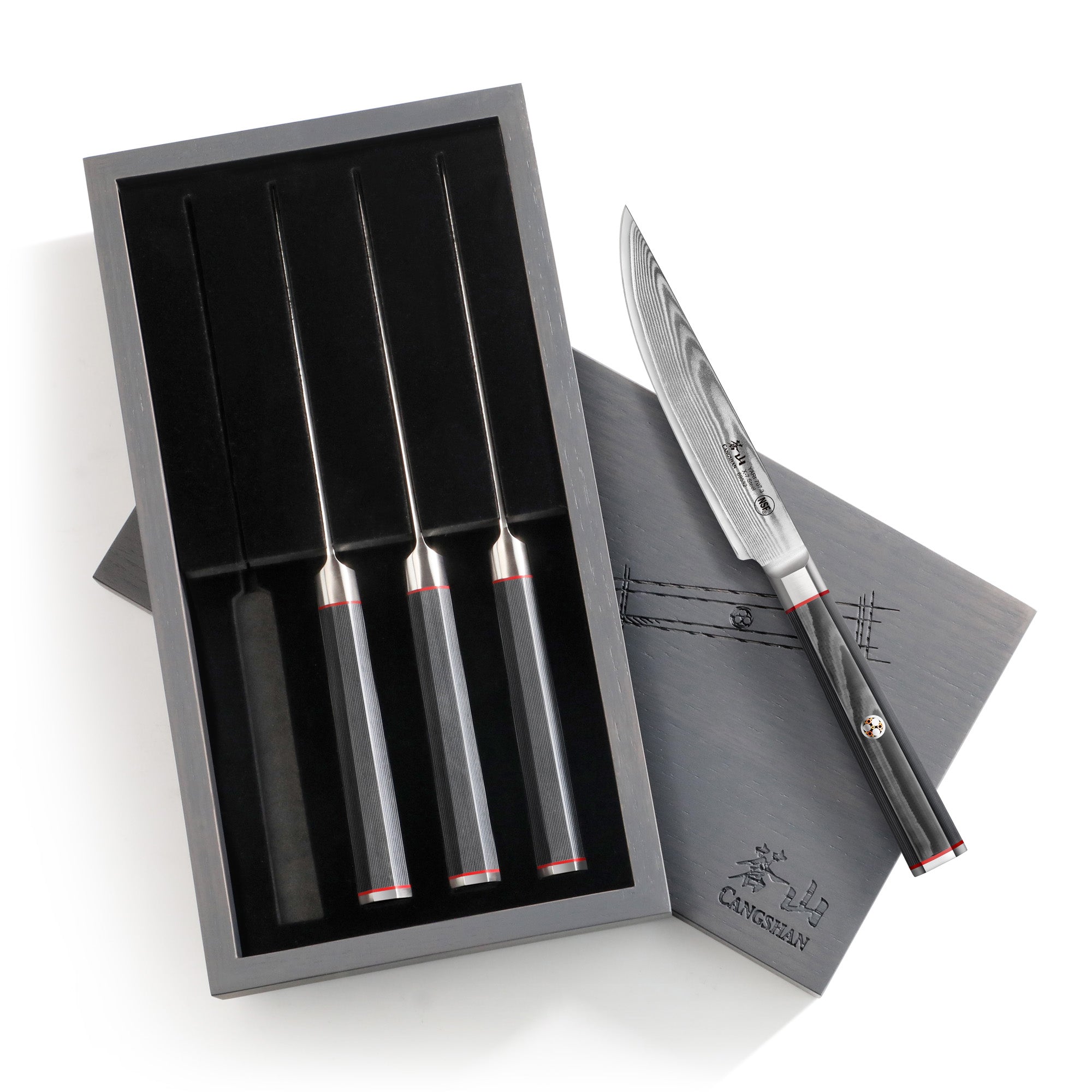 Four steak knives with black handles in a black ash wood box, one knife outside showing a patterned Damascus steel blade.