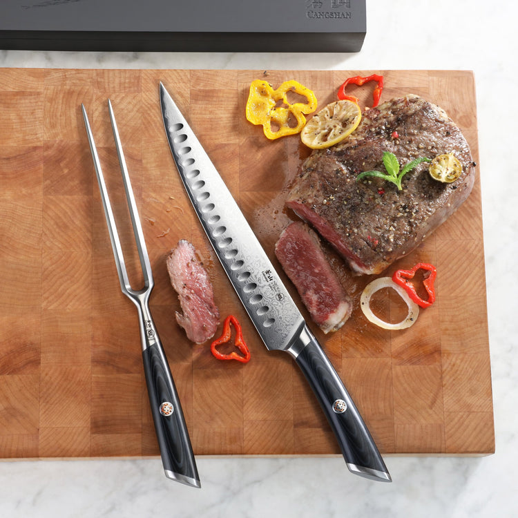 Two-piece carving knife set with a partially sliced cooked steak, garnished with lemon slices and bell pepper on a wooden cut