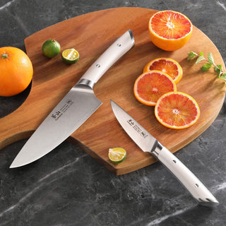 
                    
                      Two kitchen knives with white handles on a wooden cutting board beside sliced blood oranges.
                    
                  