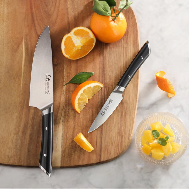 Chef knife and paring knife with black handles on a wooden cutting board with sliced oranges.