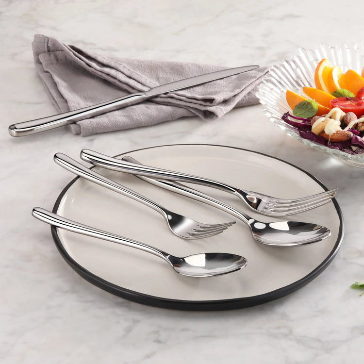 Four pieces of polished stainless steel flatware—knife, fork, tablespoon, and teaspoon—rest on a white plate with a black rim