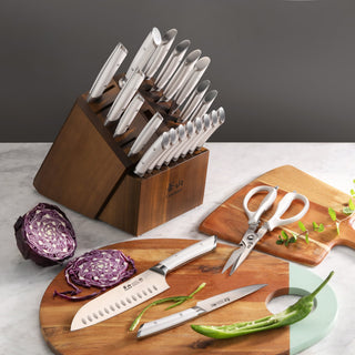 
                    
                      23-piece knife set with stainless steel blades in acacia wood block, displayed with kitchen scissors and vegetables.
                    
                  