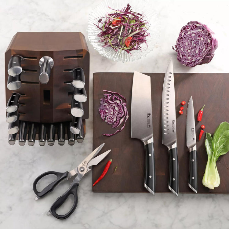 Wooden knife block with 23 knives and kitchen shears, three knives on cutting board with chopped cabbage and chili peppers.