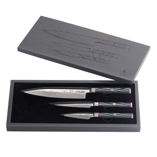 
                    
                      Three knives with patterned blades and black handles in a black box with a gray lid featuring knife sketches.
                    
                  