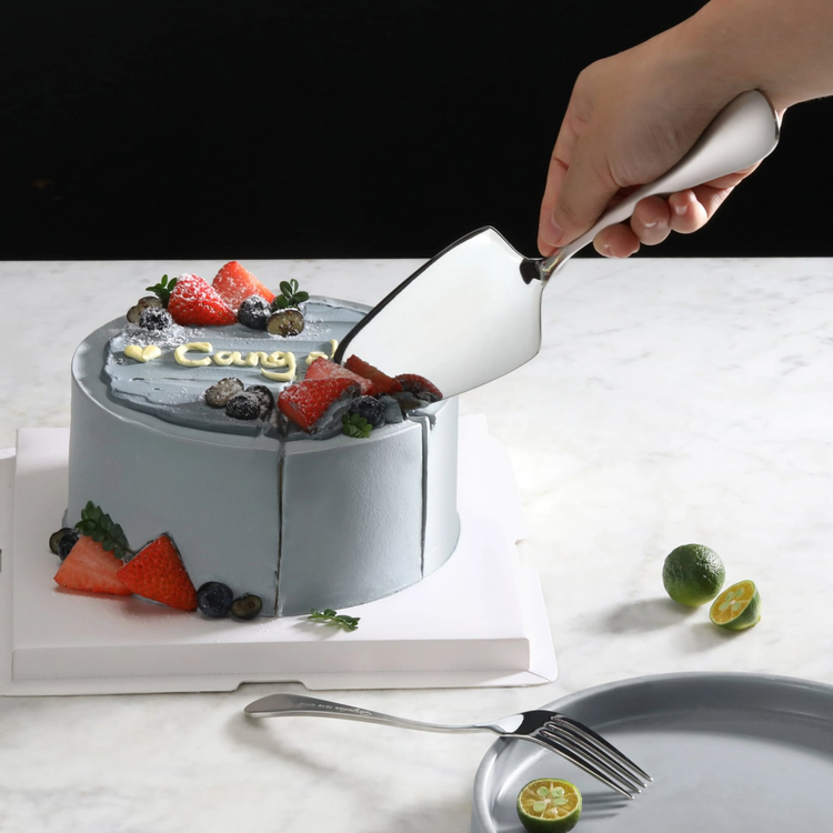 Hand holding stainless steel pie server with matte finish handles, lifting a slice from a decorated cake.