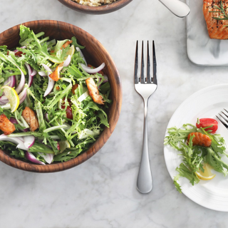 
                    
                      Serving fork with matte finish handles placed on a marble surface next to a wooden bowl of salad and a white plate with salad
                    
                  