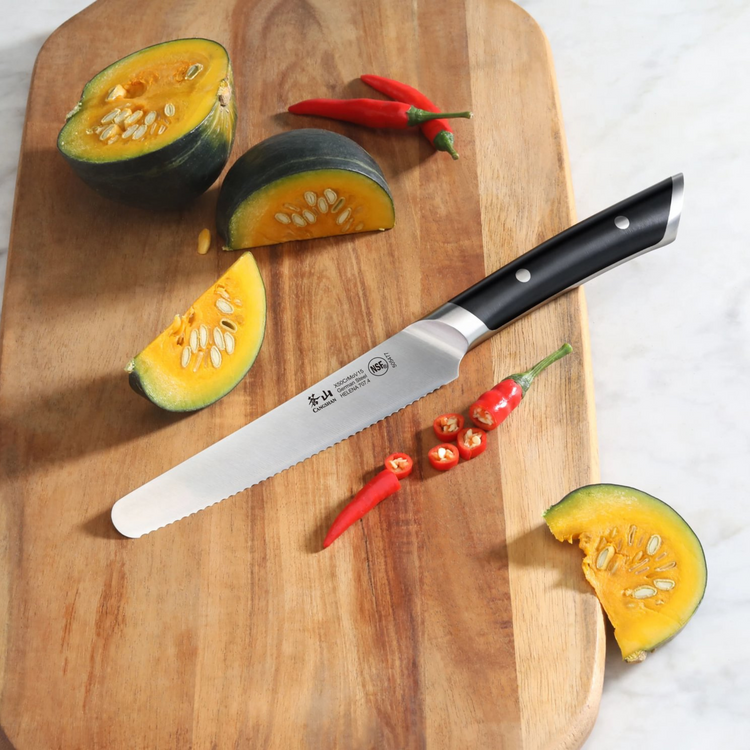 Serrated utility knife with black handle on wooden board, surrounded by sliced squash and red chili peppers.