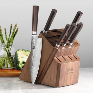 
                    
                      Wooden knife block with six knives inserted and one knife displayed on the side, placed on a kitchen counter.
                    
                  