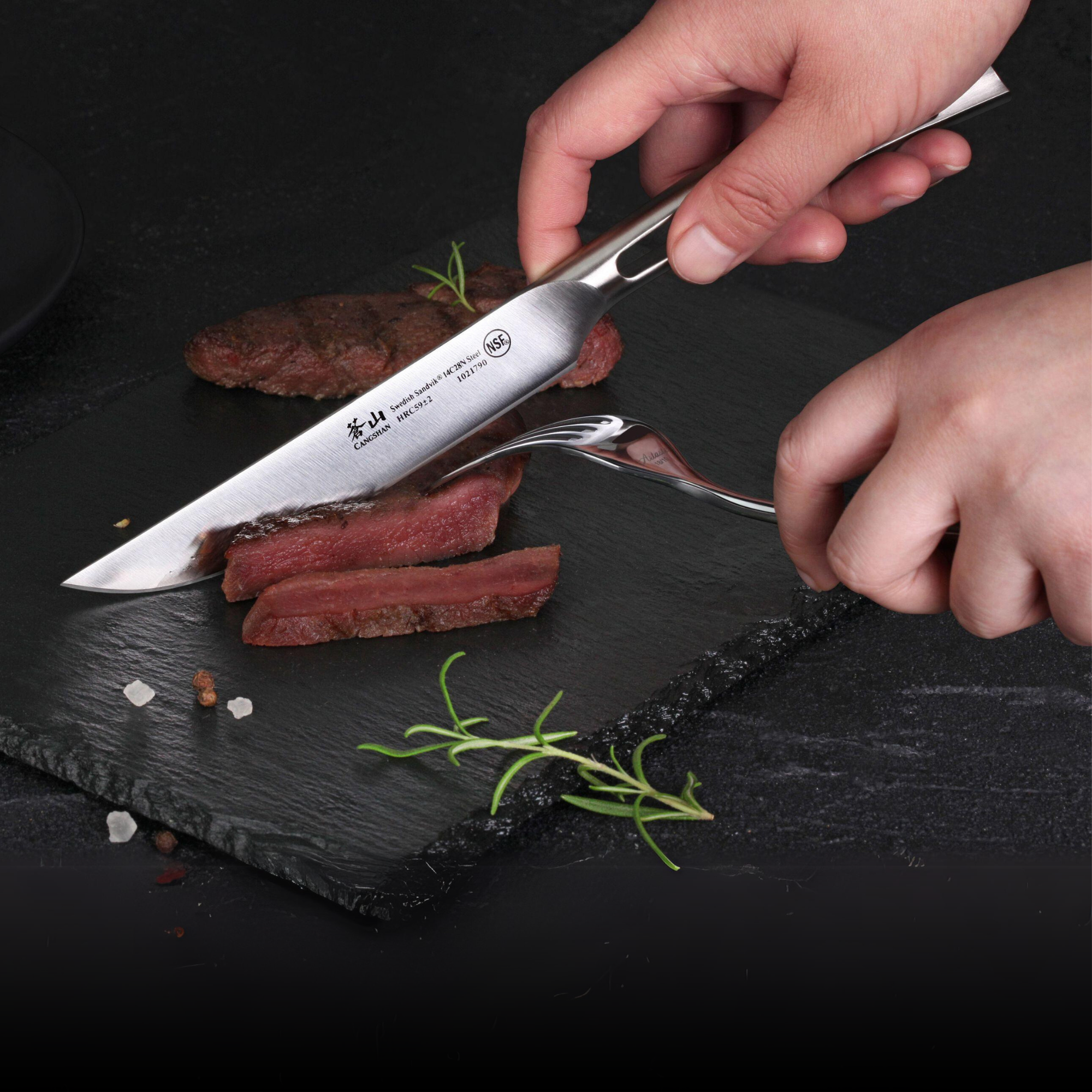 Hand using a steak knife to cut slices of cooked meat on a black slate serving board with rosemary and coarse salt.