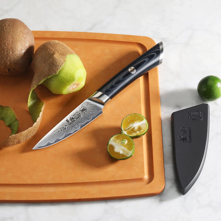 3.5-inch Damascus steel paring knife with black handle on cutting board, next to peeled kiwi and halved lime with sheath near