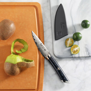 
                    
                      3.5-inch paring knife with patterned blade and black handle, next to peeled kiwi and halved limes on cutting boards.
                    
                  