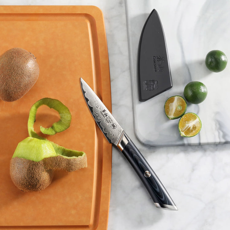 3.5-inch paring knife with patterned blade and black handle, next to peeled kiwi and halved limes on cutting boards.