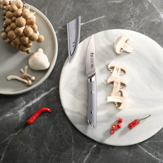 
                    
                      3.5-inch paring knife with gray handle and sheath on a marble board with sliced mushrooms and red chili peppers.
                    
                  