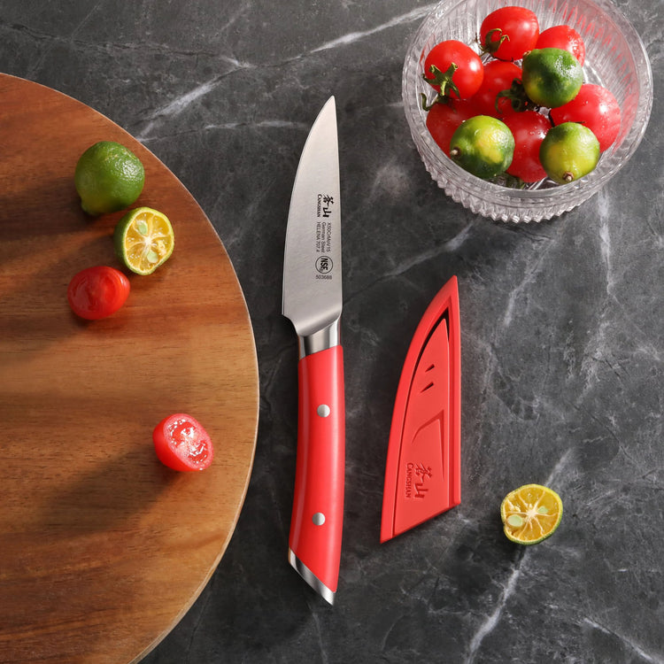 3.5-inch paring knife with red handle and matching sheath next to sliced and whole small tomatoes and limes on dark counterto