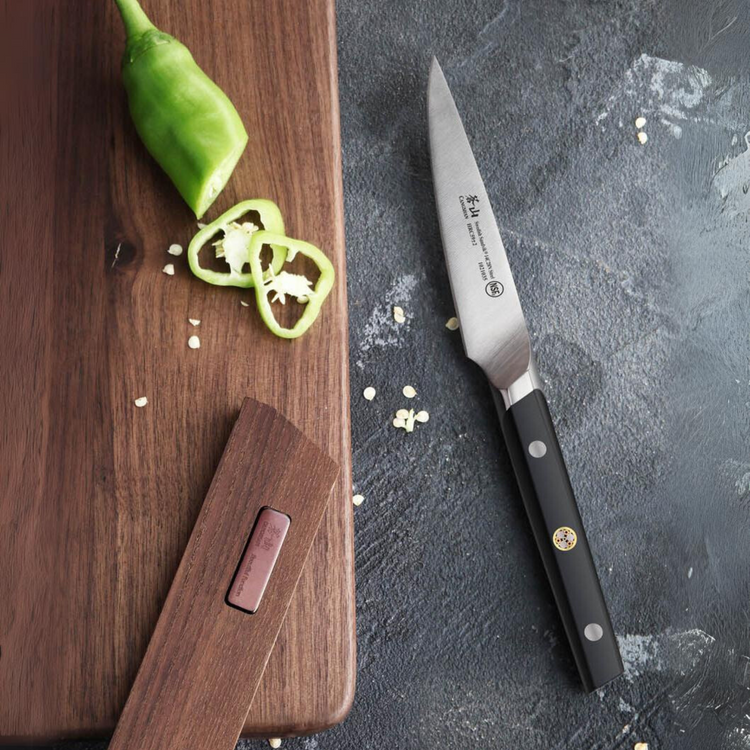 Sliced green chili pepper on a wooden cutting board next to a paring knife on a dark countertop.