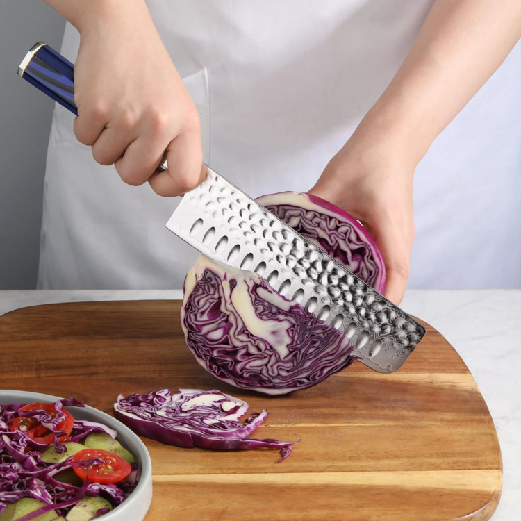 Hand holding a knife slicing a halved purple cabbage on a wooden cutting board next to a bowl of salad.