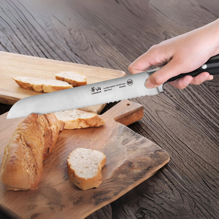 Hand holding a serrated bread knife cutting a loaf of bread on a wooden cutting board.