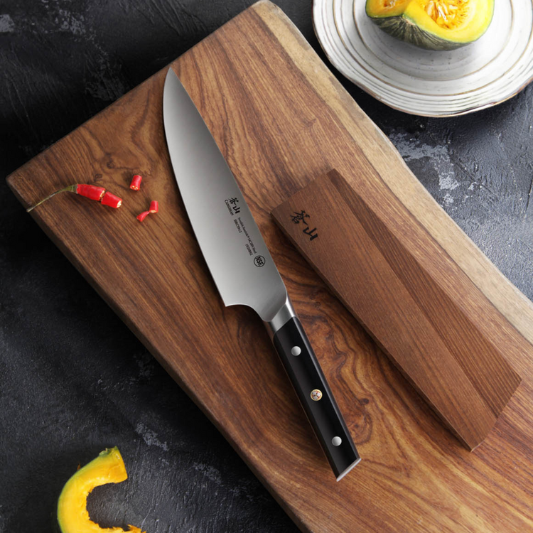 8-inch chef knife with black handle and wooden sheath on a wooden cutting board with sliced chili and squash.