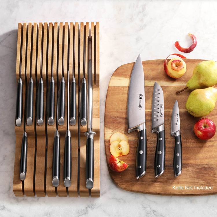 Bamboo knife organizer with 15 slots holding knives, next to a cutting board with three knives and assorted fruit.