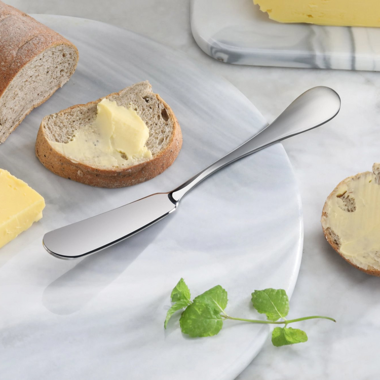 Stainless steel butter knife with matte finish handle on marble board next to bread slices with butter.