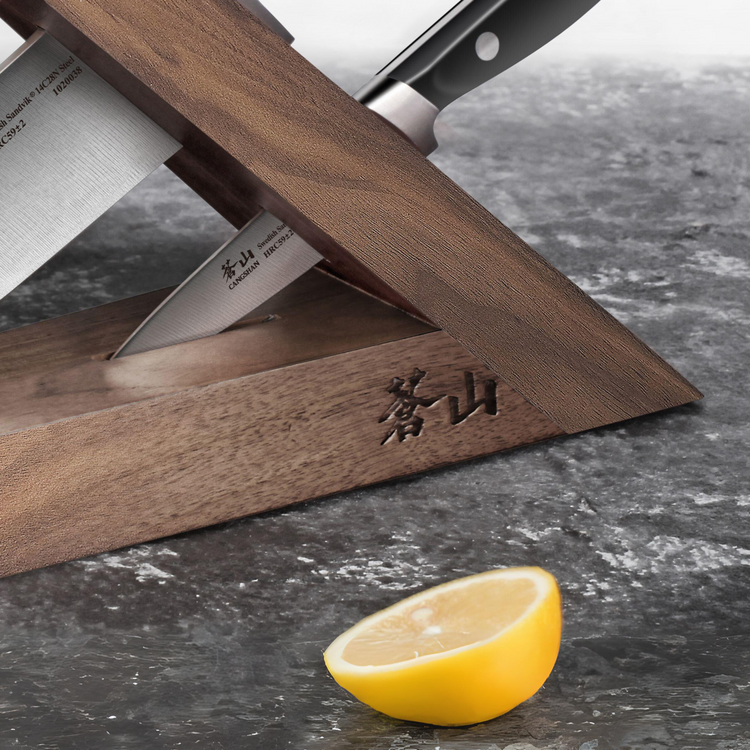 Walnut wood triangular knife block holding two knives on a gray countertop with half a lemon nearby.