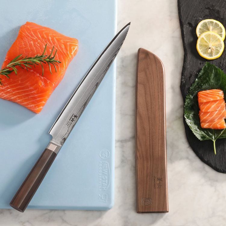 Walnut magnetic knife sheath next to a Japanese-style knife and salmon on a cutting board and slate plate.