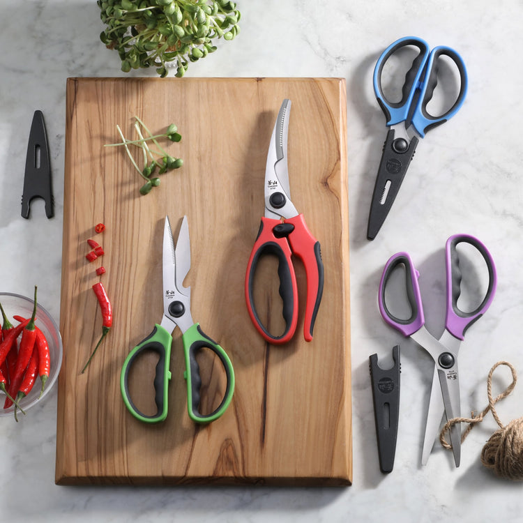 Four pairs of colorful kitchen shears with black blade guards, displayed on and beside a wooden cutting board.