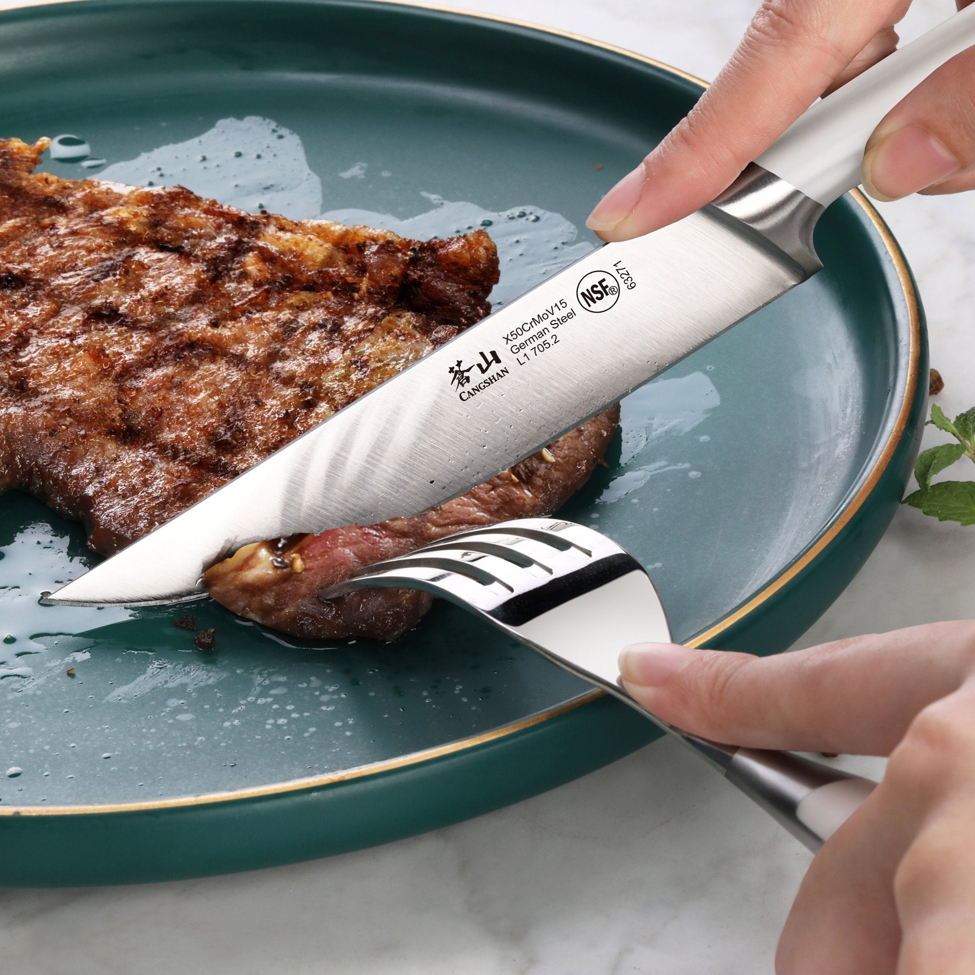 Hand holding a steak knife cutting a grilled steak on a teal plate, with a fork securing the meat.