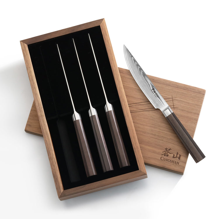 Four steak knives with dark wooden handles in a wooden box, one knife placed outside on the box lid.