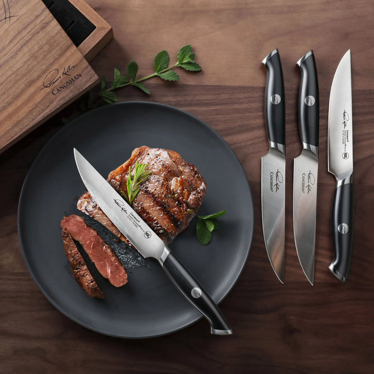 Four black-handled steak knives with stainless steel blades next to a plate holding a cooked steak and sliced pieces.