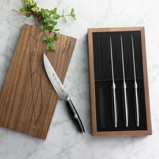 
                    
                      Four 5-inch steak knives with black handles in a walnut storage box, one knife outside on a wooden lid.
                    
                  